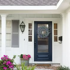 a blue front door with purple flowers on the side and green planters in front