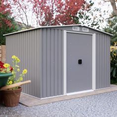 a small gray shed sitting in the middle of a yard next to some flowers and potted plants