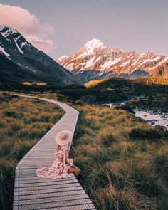 a woman sitting on a wooden walkway in front of snow covered mountains and a river