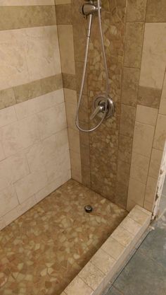 a walk in shower sitting next to a tiled wall and floor with a hand held shower head