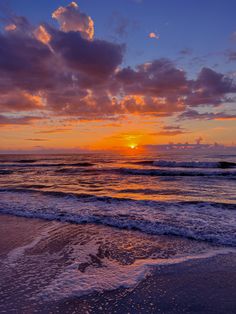 the sun is setting over the ocean with clouds in the sky and waves on the beach