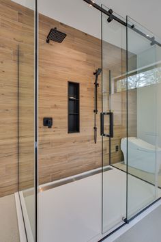 a bathroom with a glass shower door and wooden wall behind the bathtub is a toilet