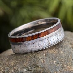 a wedding band with wood inlays sits on top of a rock