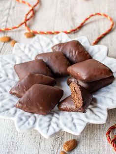 several pieces of chocolate on a white plate with nuts and string in the foreground