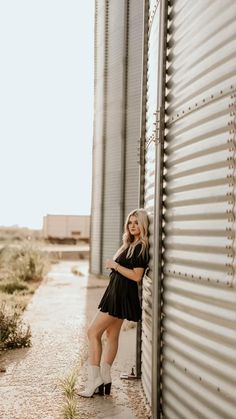 a woman leaning against the side of a metal building with her legs crossed and wearing white boots