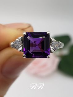 Made to order.  Please allow up to 3 weeks for the production of your ring. This listing is for a 925 non-plated sterling silver or non-plated gold ring with a natural dark purple amethyst asscher cut center stone in the size of your choosing. Photos show the 8mm sterling silver. Amethyst Asscher Cut Center Stone Sizes 7mm (2 Carat Approximately) 8mm (2.5 Carat Approximately) Center Stone Gem Type: Natural Amethyst Shape: Asscher Cut Size: Your Choice Color: Dark Purple Quality: AAA Hardness: 9 Mohs Accent Stones Gem Type: Lab Created Cubic Zirconia Diamonds Shape: Trillion Cut Size: (2) 4mm Color: White Colorless Quality: 6A Hardness: 8.5 Mohs Metal Selection (all metals are solid and non-plated) 925 Sterling Silver 10KT White Gold (non-rhodium plated) 10KT Yellow Gold 14KT White Gold (no Classic Amethyst Ring With Cubic Zirconia For Gift, Classic Cubic Zirconia Amethyst Ring For Gift, Gift Amethyst Ring With Round Cut And Vs Clarity, Gift Amethyst Ring With Vs Clarity Round Cut, Gift Amethyst Ring Vs Clarity Round Cut, Classic Amethyst Ring With Vs Clarity As A Gift, Classic Purple Solitaire Jewelry, Classic Amethyst Gift Ring, Luxury Purple Jewelry For Anniversary