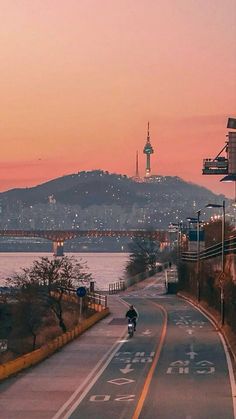 a person riding a bike down a street next to the ocean at sunset with a bridge in the background