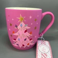 a pink coffee cup with a christmas tree on it next to a card and tag