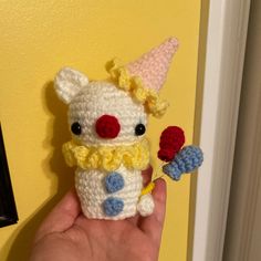 a small crocheted toy with a clown hat on it's head holding a flower