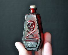 a hand holding a red glass bottle with a skull and crossbones on it