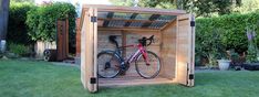 a bicycle is parked in a wooden storage shed with grass and bushes behind it,