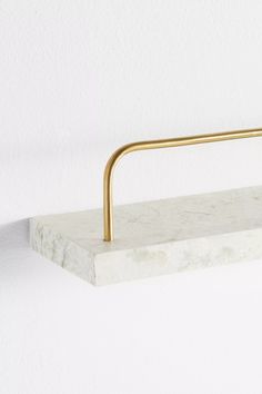 a white marble shelf with a gold metal handle on the top, against a white wall