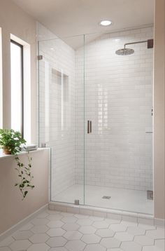 a white tiled bathroom with a glass shower door and window above the sink is a potted plant