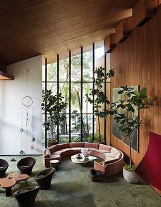 a living room filled with lots of furniture next to a tall wooden wall covered in windows