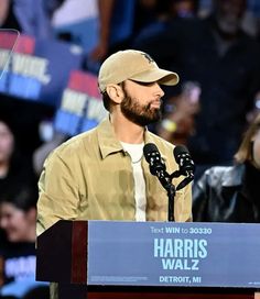 a man standing at a podium with a baseball cap on and microphone in front of him