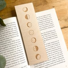 a bookmark with four phases of the moon on it sitting next to an open book