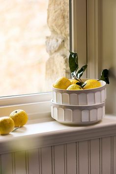 a white bowl filled with lemons on top of a window sill