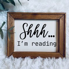 a wooden frame with the words shh i'm reading in black ink on it