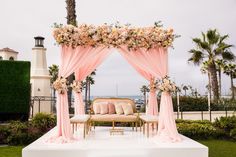 an outdoor ceremony setup with pink drapes and flowers on the altar, along with two gold chairs