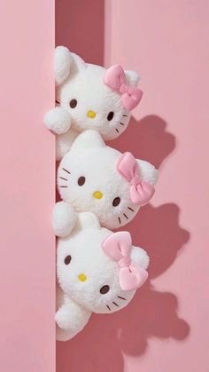 three hello kitty stuffed animals are hanging on a pink wall with shadows from the walls