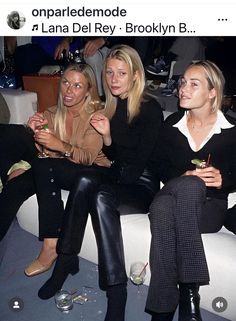 three women sitting next to each other on a couch with drinks in front of them