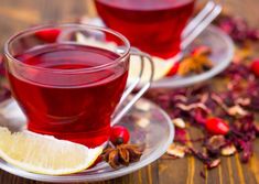 two cups filled with red tea sitting on top of a plate next to some fruit