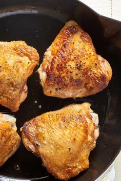 four pieces of chicken cooking in a skillet