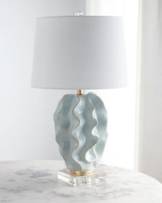 a white lamp sitting on top of a table next to a window with curtains behind it