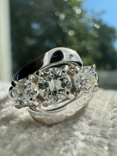 three stone diamond ring sitting on top of a white furnishing with trees in the background