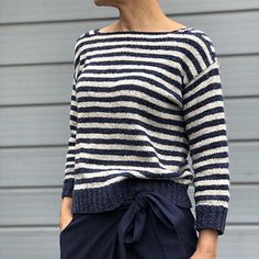 a woman with short hair wearing a striped sweater and navy blue shorts is standing in front of a gray wall