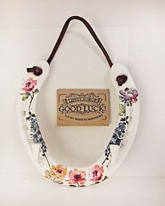 a white flowered wreath hanging on a wall with a brown cord and a sign that says good luck