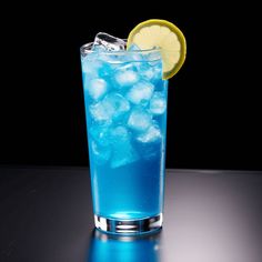 a blue drink with ice and lemon wedges on the rim, in front of a black background