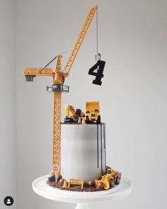 a birthday cake with construction trucks and cranes on top is displayed in front of a white wall