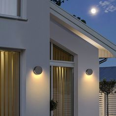 two lights on the side of a white building at night with a full moon in the background