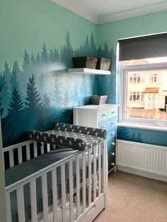 a baby's room decorated in teal and white with trees painted on the wall