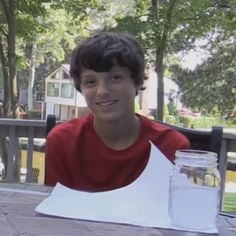 a young man sitting at a table with a jar of water and paper on it