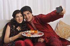 a man and woman sitting on a couch taking a selfie with a plate of food