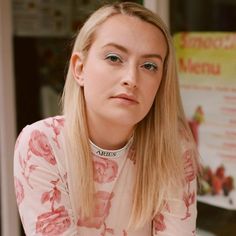 a woman with long blonde hair and blue eyes is sitting in front of a sign