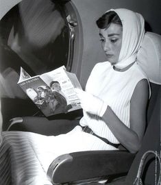 a woman reading a magazine while sitting in an airplane with her head covering over her face