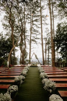 an outdoor ceremony setup with wooden benches and flowers on the aisle leading up to it