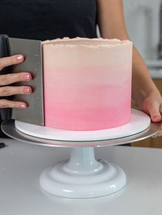 a woman is holding a pink and white cake