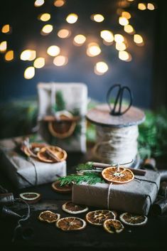 a table topped with wrapped presents next to twine and christmas lights in the background