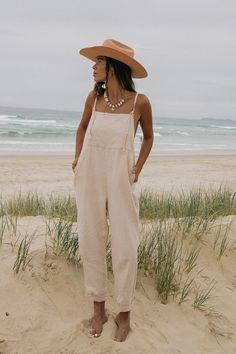 A woman standing on a beach in front of the ocean, wearing a wide-brimmed hat, necklace, and light pink overalls over a tank top. Rose Jewellery, Sustainable Accessories, Organic Plant, Toxic Free, Plant Dyes, Organic Plants, 21 Days, Layered Look, Font Size