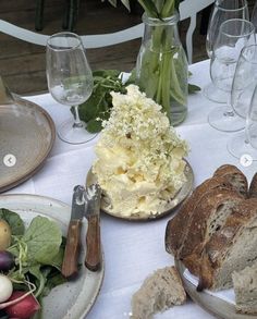 a table topped with bread and vegetables next to wine glasses on top of a white table cloth