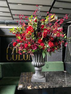 a vase filled with red flowers sitting on top of a marble table next to a green bench