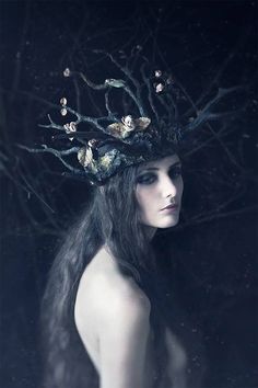 a woman with long black hair and a crown on her head is standing in the dark