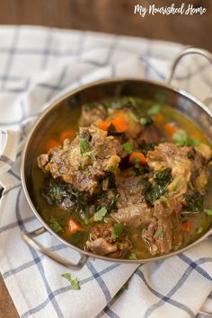 a pot filled with meat and vegetables sitting on top of a white table cloth next to a spoon