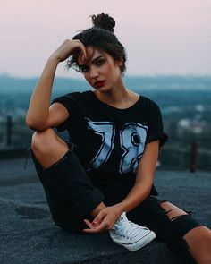 a woman sitting on top of a roof with her hands behind her head and looking at the camera