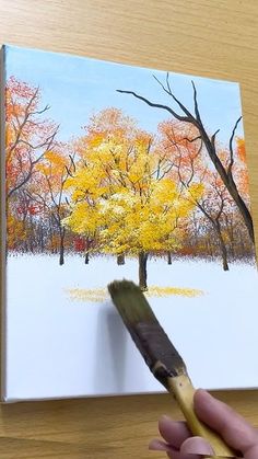 someone is holding a paintbrush in their hand and painting a tree with yellow leaves