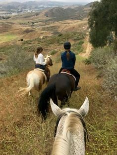 two people are riding horses through the hills